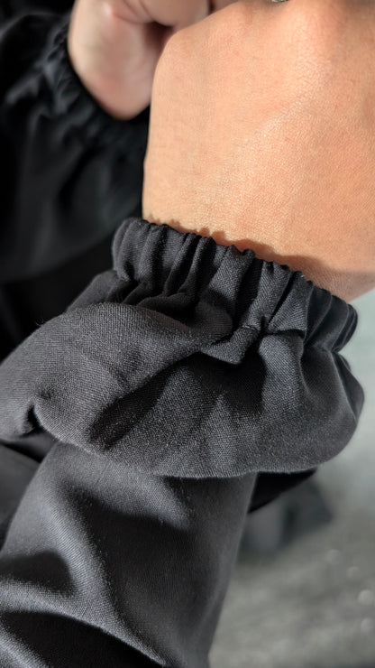 Close-up of a black long-sleeve top with a gathered elastic cuff on a person's arm.