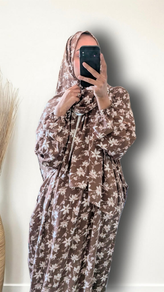 A person taking a mirror selfie wearing a brown and beige floral print kaftan dress and matching headscarf, holding a black smartphone to block the face.