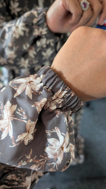 Close-up of a person's wrist and hand wearing a dark brown floral long-sleeve top with a gathered elastic cuff.