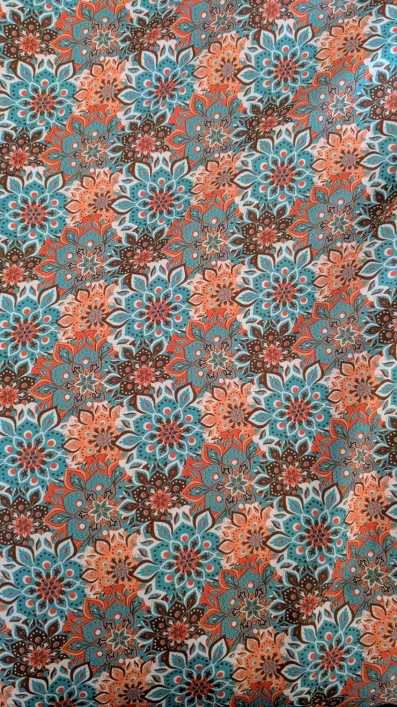 A close-up of a fabric or wallpaper pattern featuring repeating floral medallions in teal blue, coral orange, dark brown, and off-white.