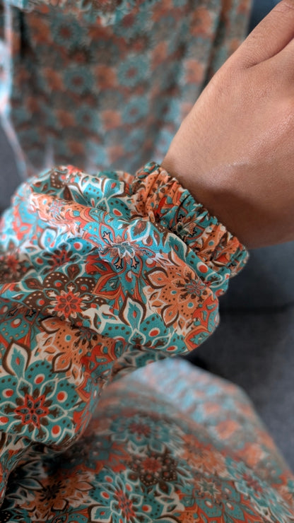 Close-up of a person's hand and wrist wearing a long, gathered sleeve with a teal, rust orange, and brown floral paisley pattern.